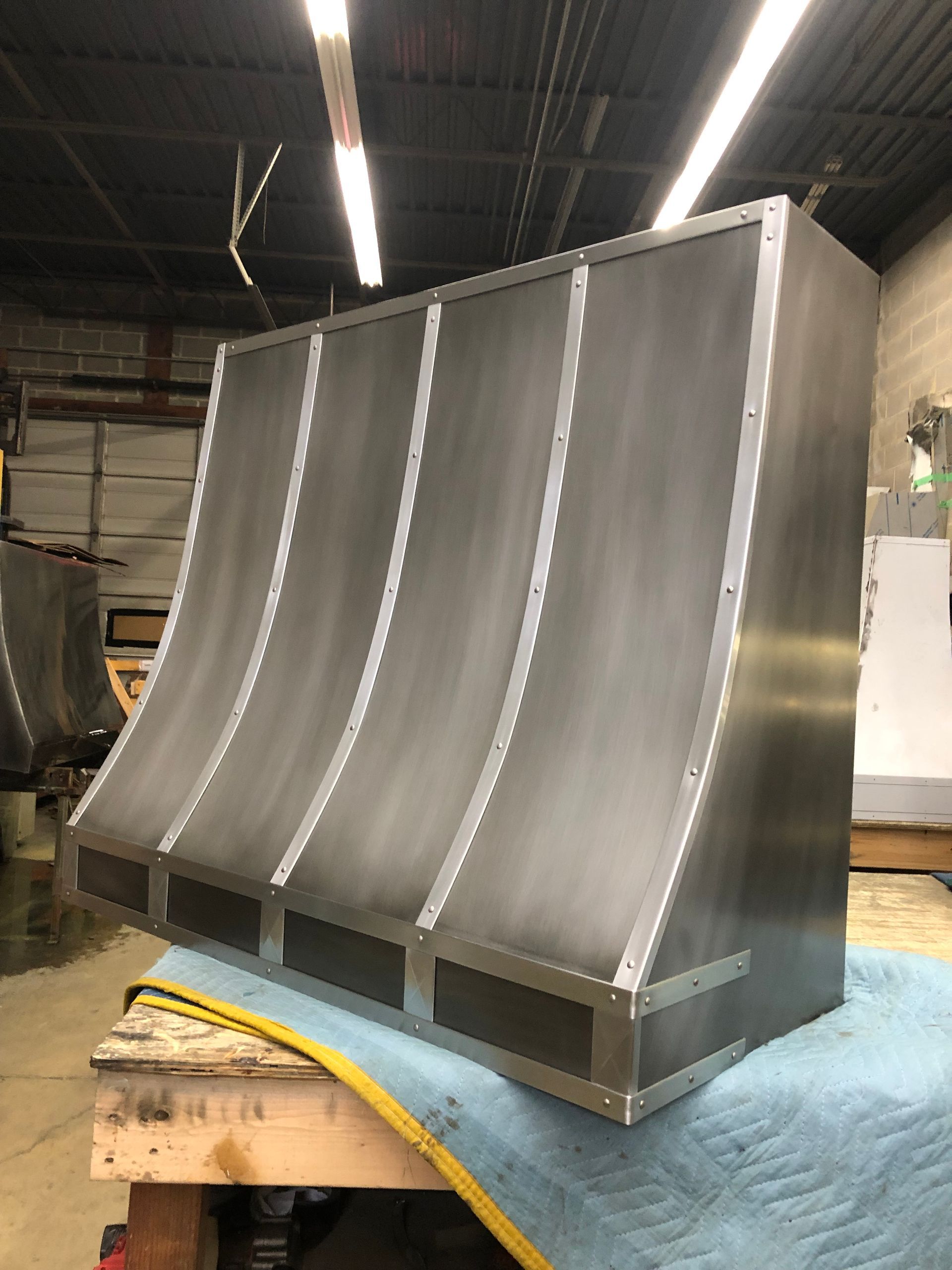 Large gray industrial metal component with curved panels, resting on a workbench in a workshop.