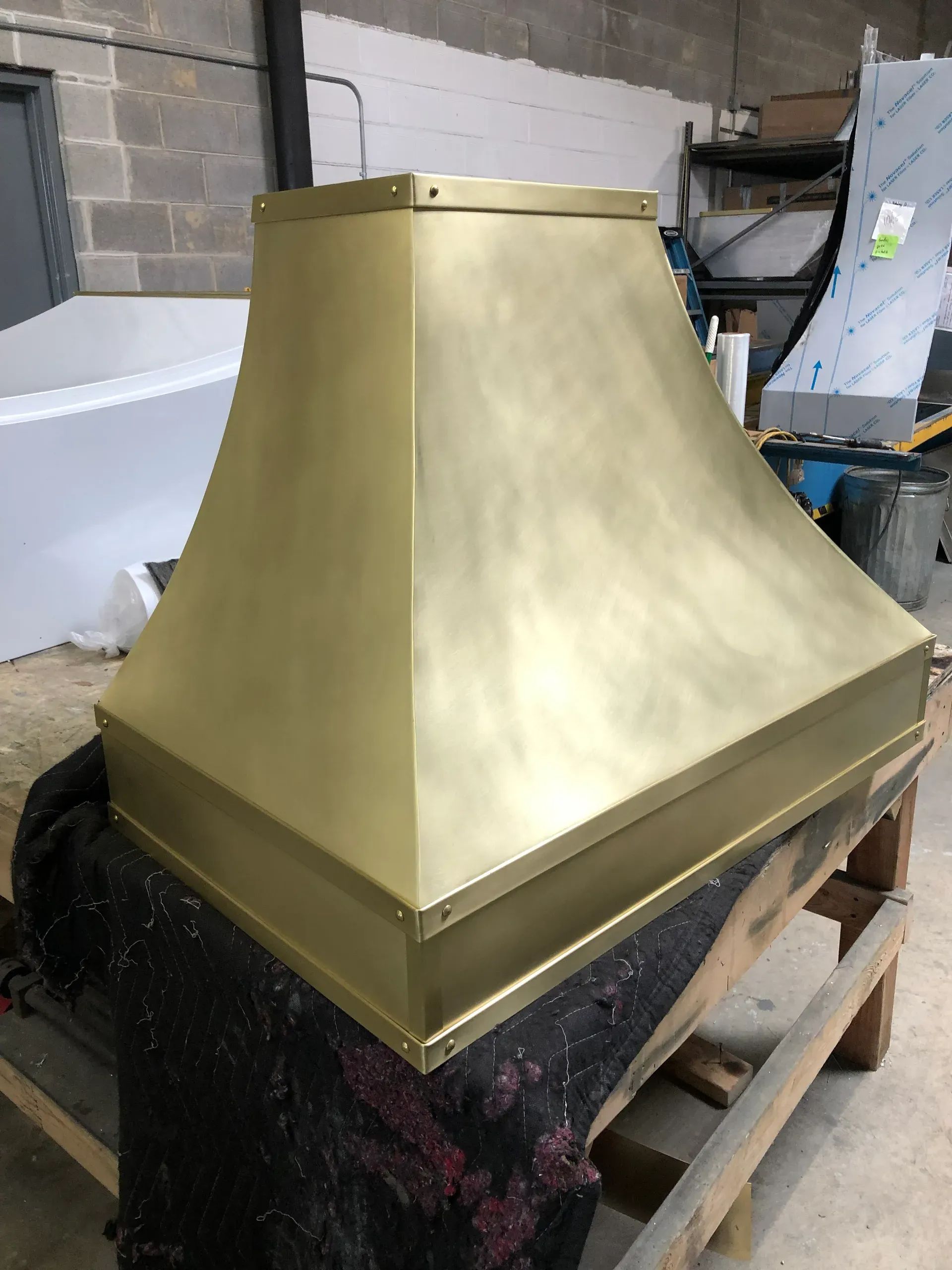 Brass-colored metal hood on a workbench in a workshop, with cinder block walls and tools in the background