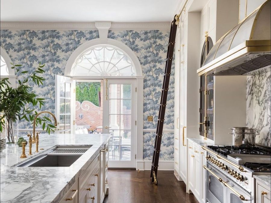 Bright kitchen with blue floral wallpaper, marble island, white cabinets, and a large arched door to a patio.