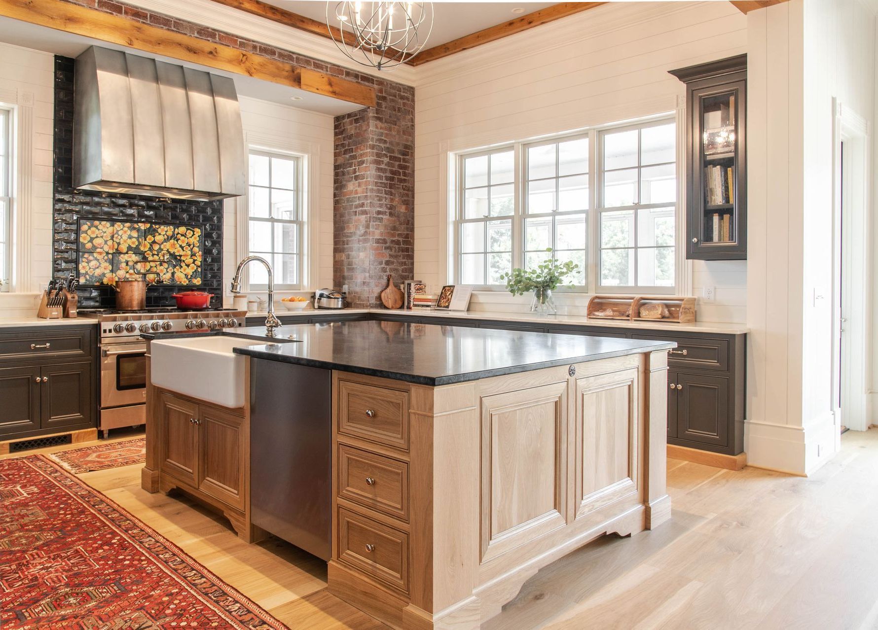 Bright modern kitchen with dark island, large windows, brick accents, and warm wood flooring