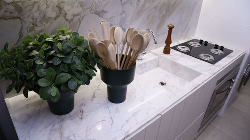 Kitchen counter with potted herbs and wooden utensils beside a stovetop and sink