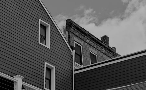 Black-and-white view of house roofs and siding with windows against a cloudy sky