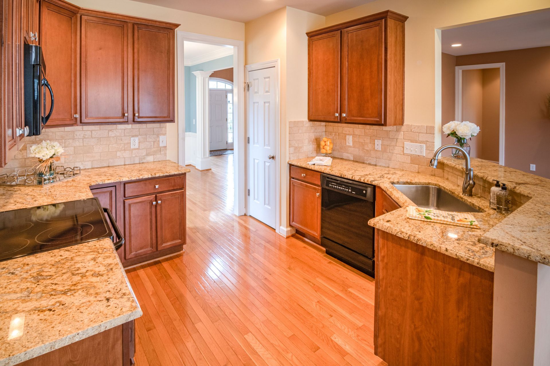 Modern kitchen with wooden cabinets, granite countertops, stainless sink, and hardwood floors.