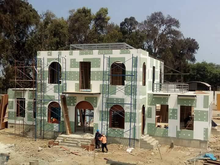 Personas trabajando juntas al aire libre, cavando la tierra con herramientas cerca de un edificio rural