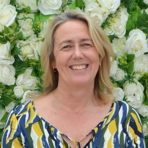 A woman is smiling in front of a wall of white flowers
