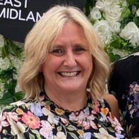 A woman with red hair is smiling in front of a wall of white flowers