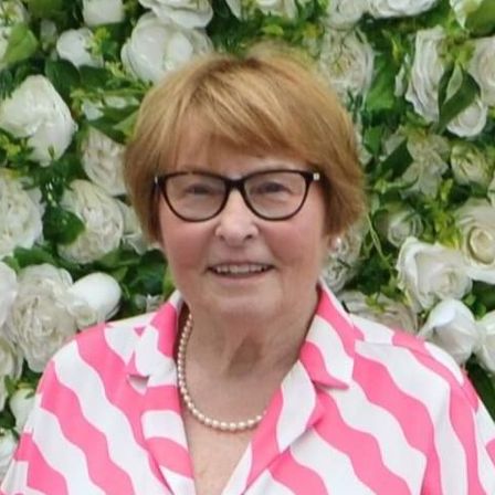 A woman with red hair is smiling in front of a wall of white flowers