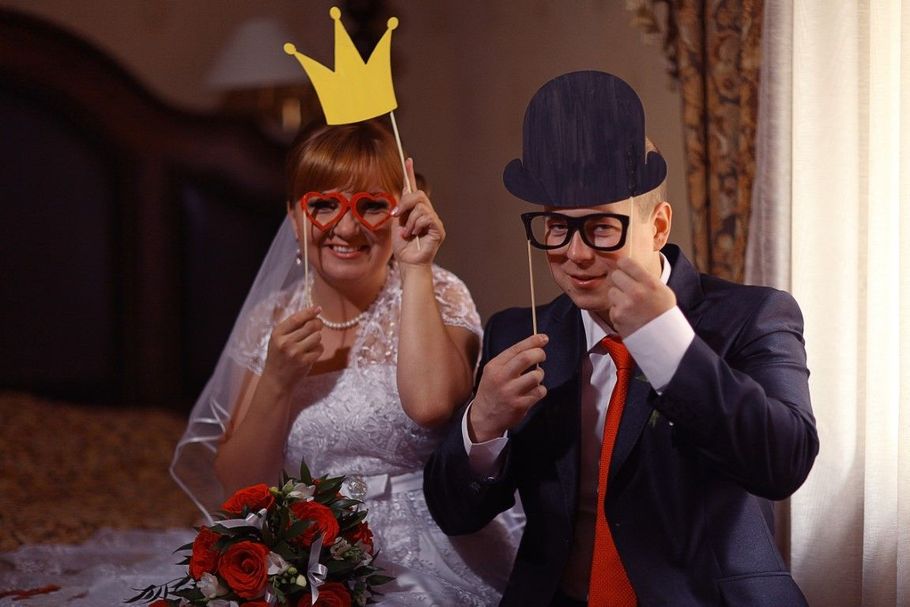 Bride and groom in paper crowns and hats pose with playful hand gestures at a wedding table
