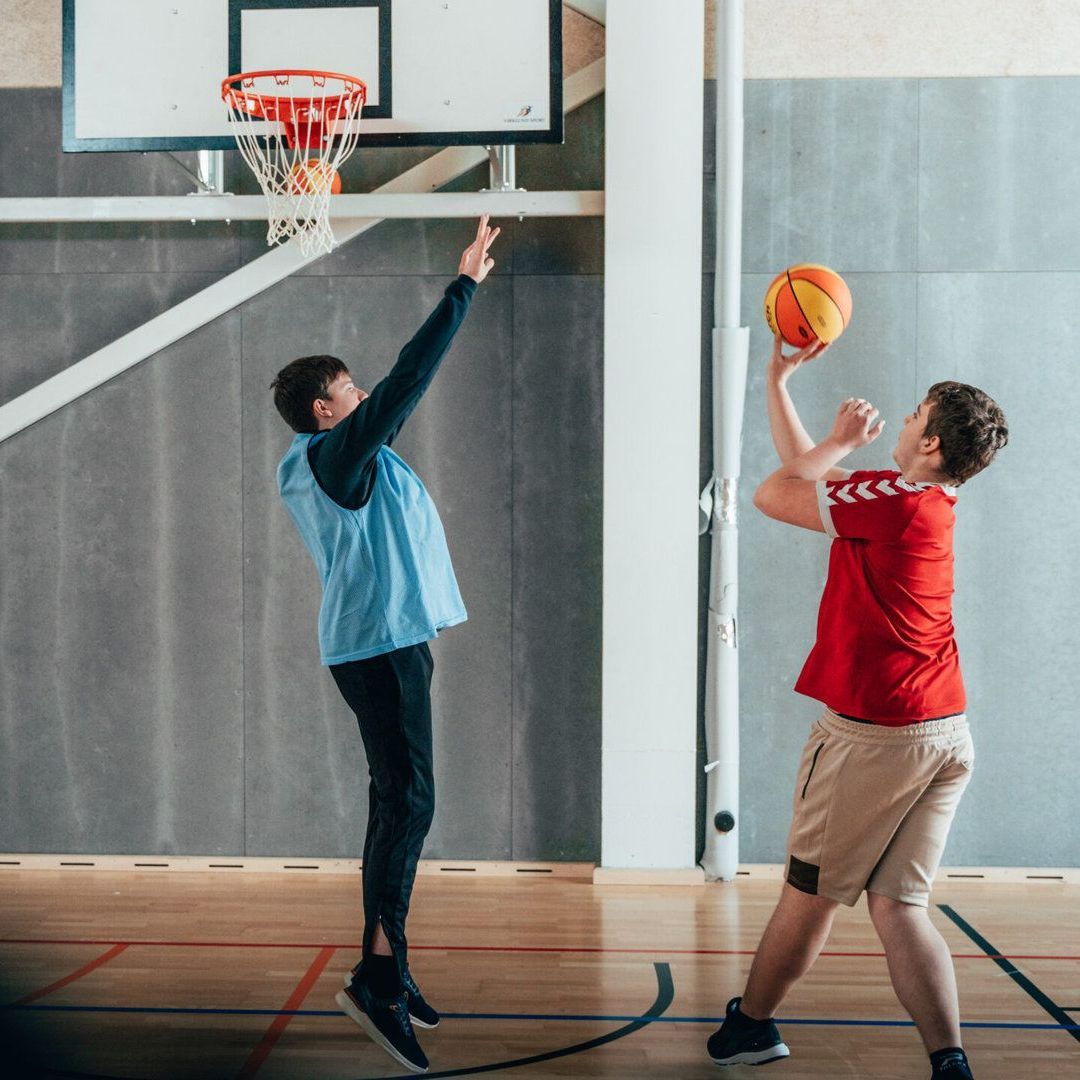 To unge mænd spiller basketball i en sportshal.