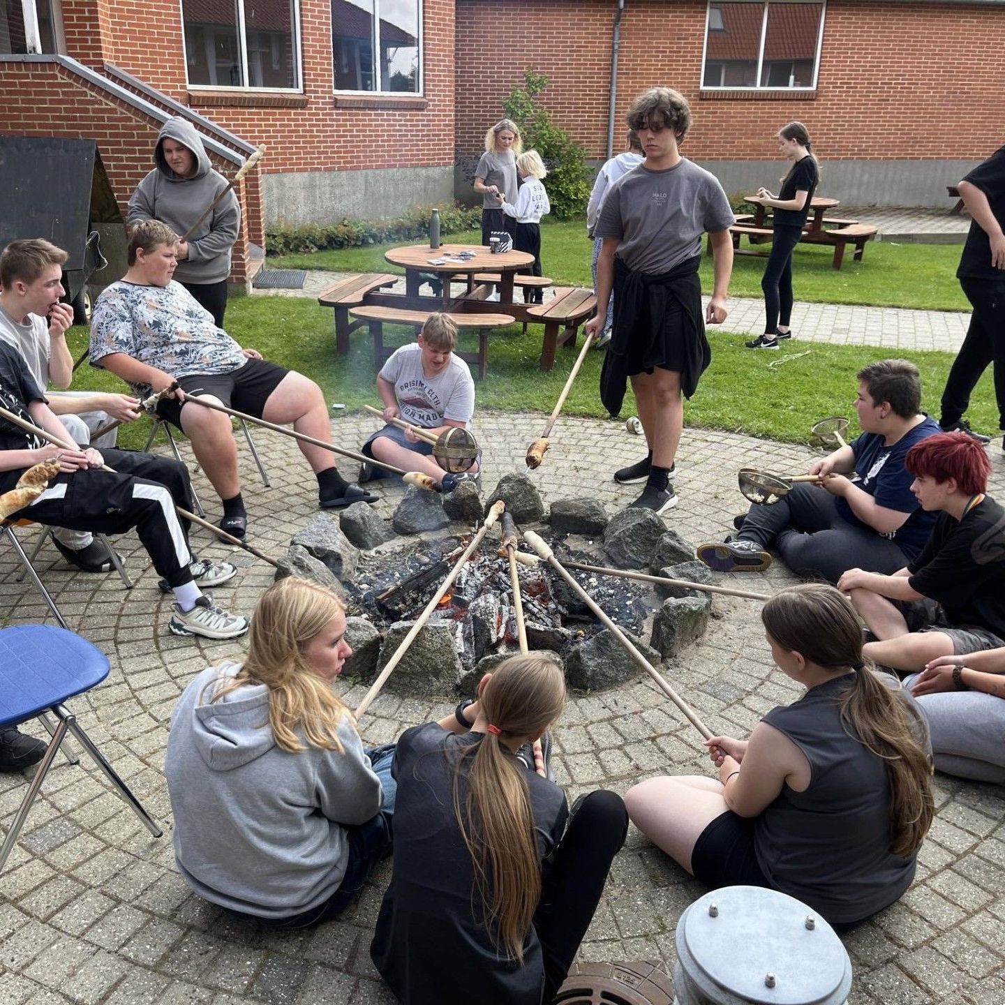 En gruppe mennesker sidder omkring en bålplads.