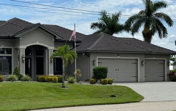 Single-story suburban house with gray roof, two-car garage, and American flag on a manicured lawn