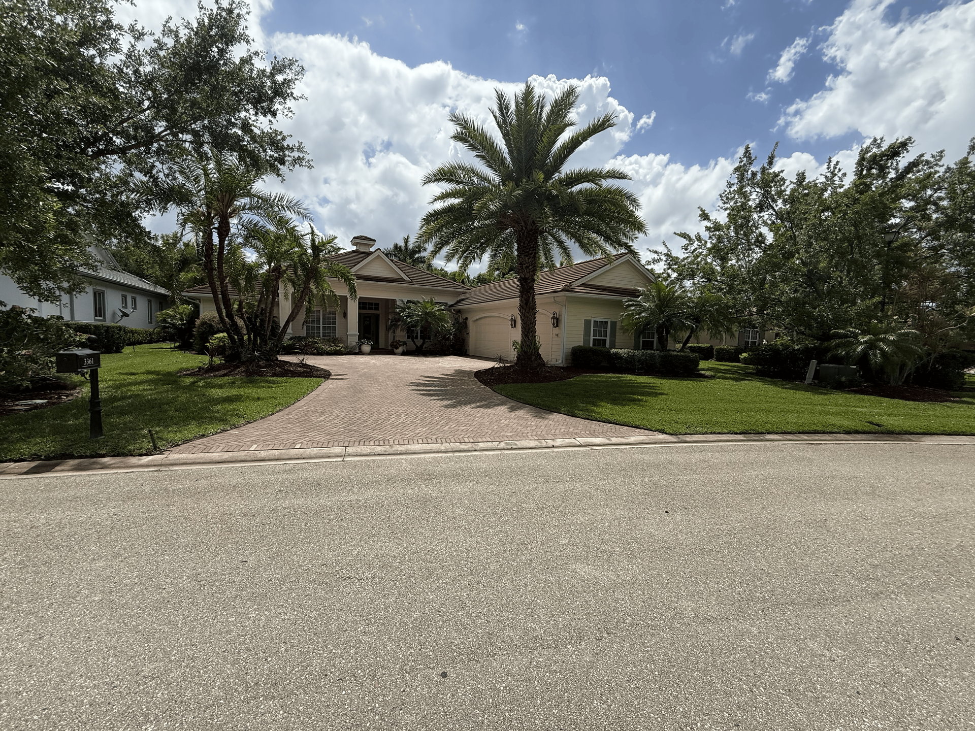 Suburban home with a palm tree, driveway, and lush green landscaping under a partly cloudy sky