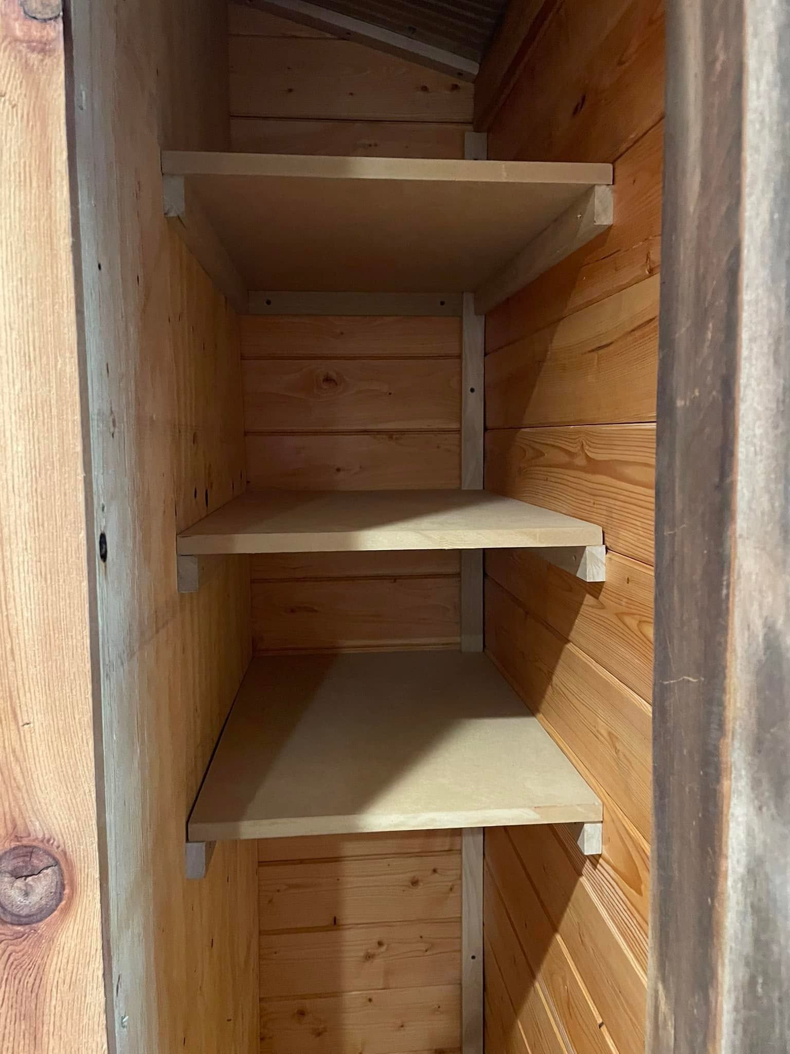 Wooden cabinet interior with four beige shelves and vertical side panels