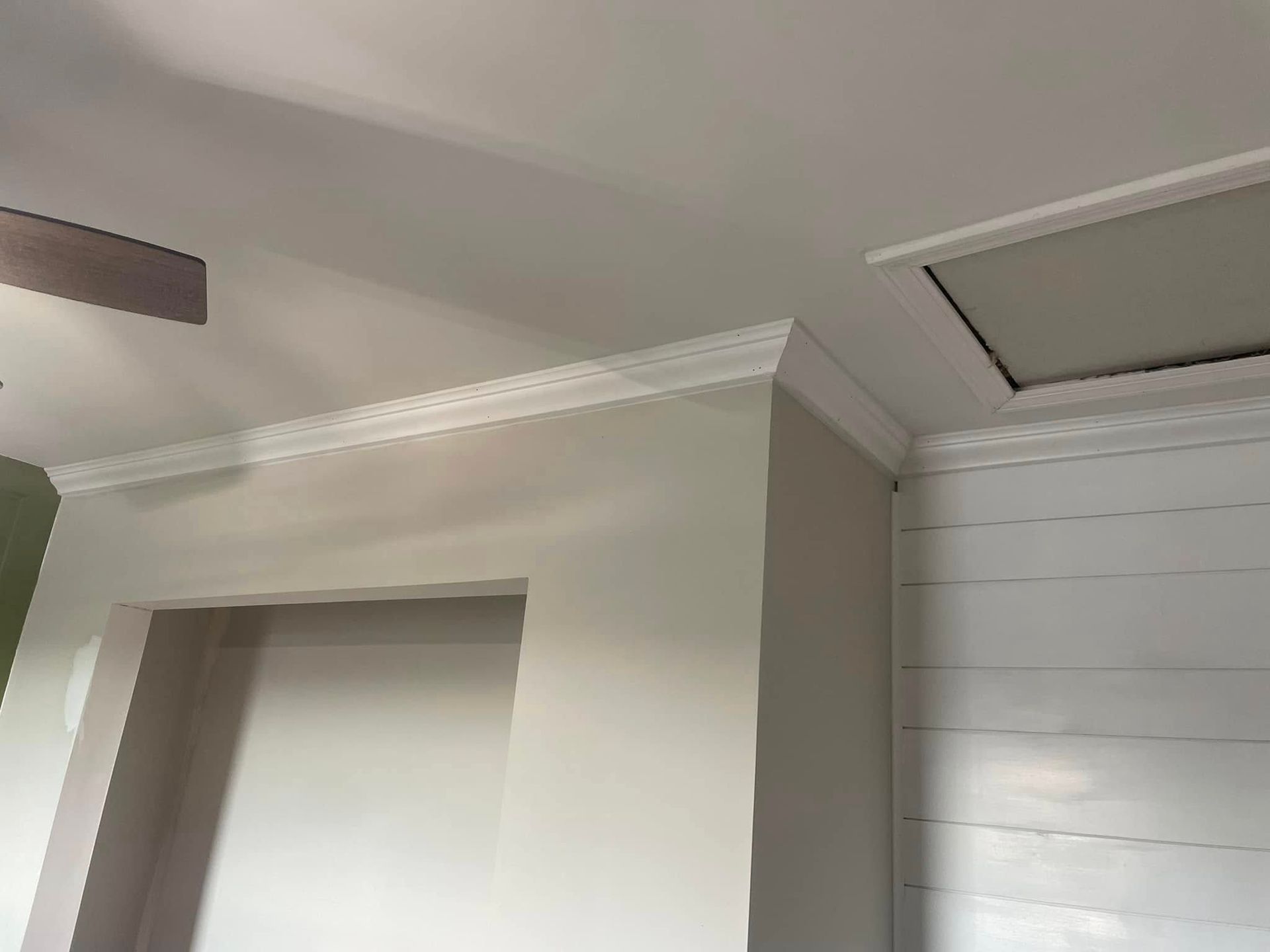 Interior ceiling corner with crown molding, a doorway, and an attic access hatch.