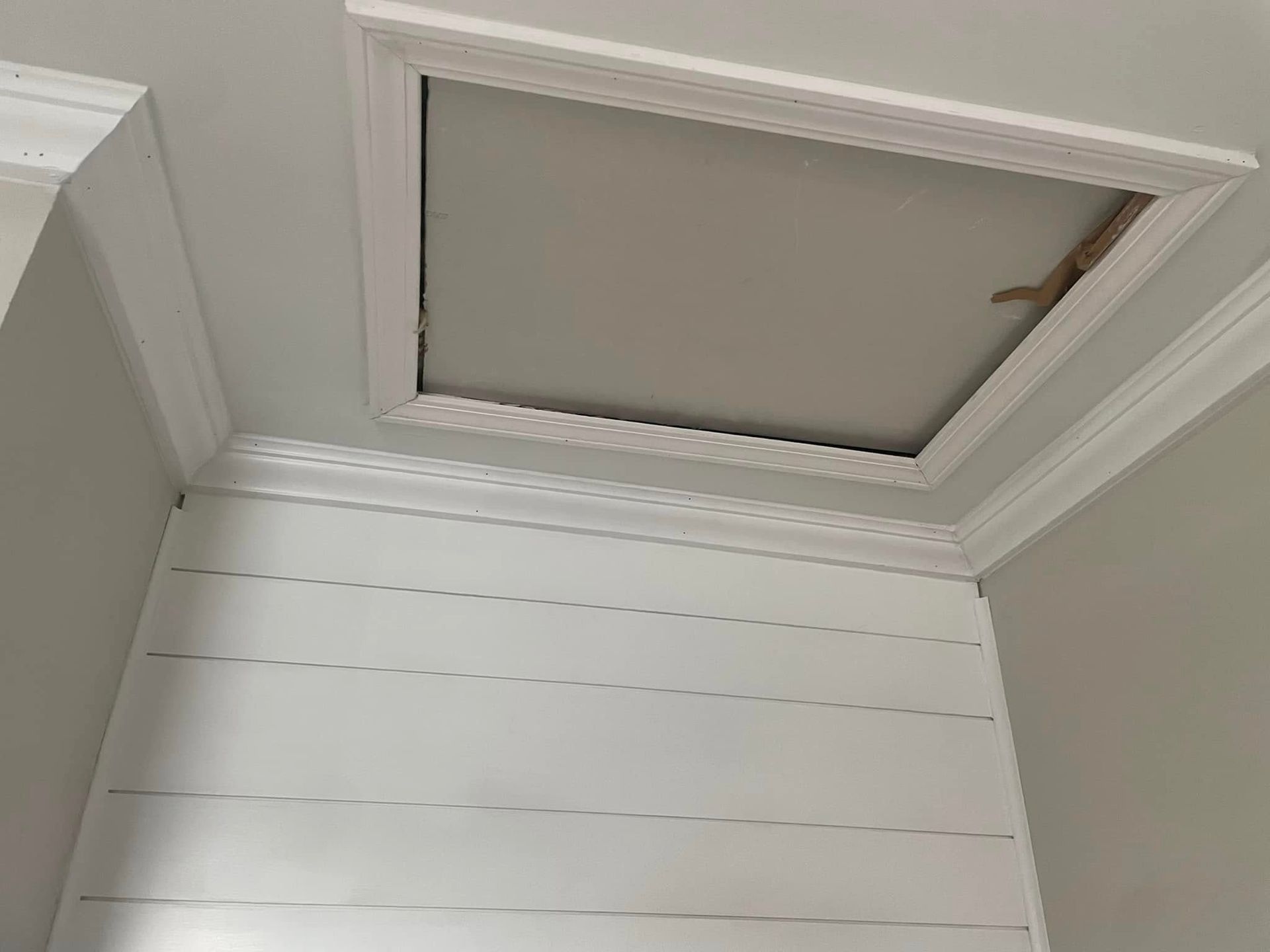 White paneled wall and ceiling corner with a small attic access panel.