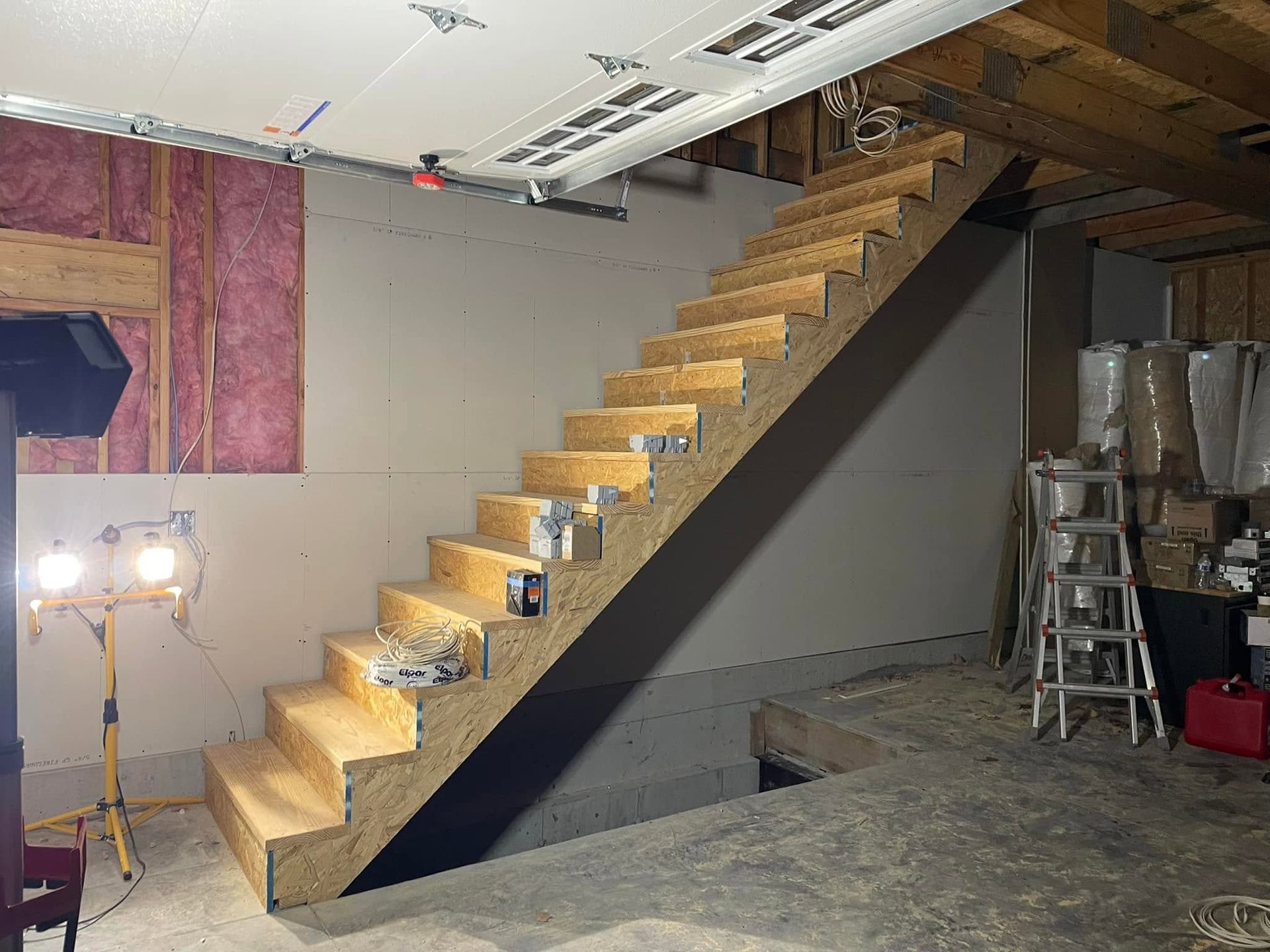 Indoor construction site with a narrow unfinished wooden staircase along a gray wall