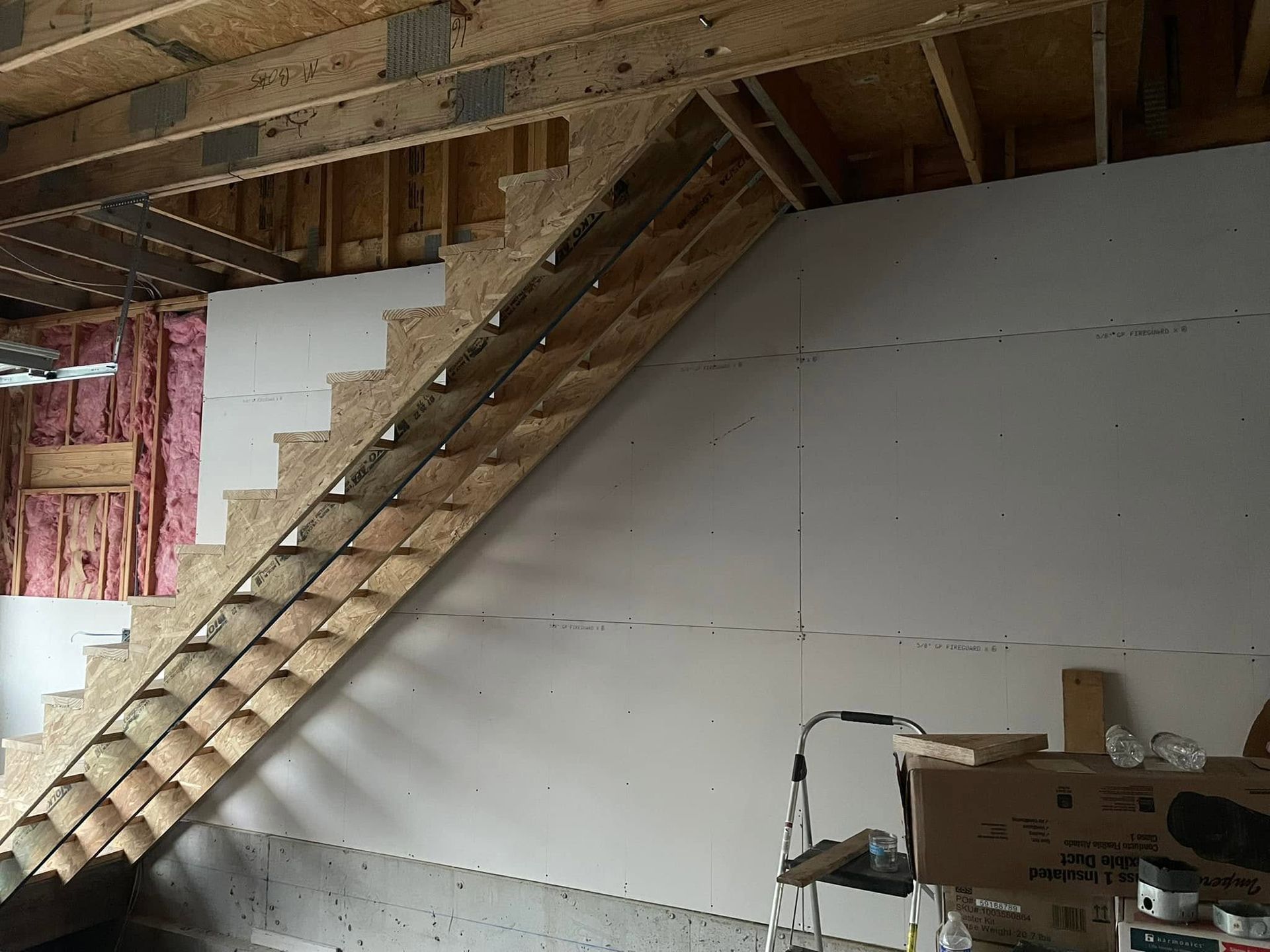 Unfinished basement with a wooden staircase, exposed insulation, and drywall under construction