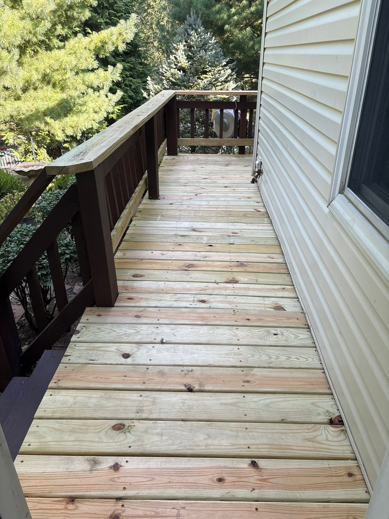 Wooden porch deck beside a house, with a railing and trees alongside.