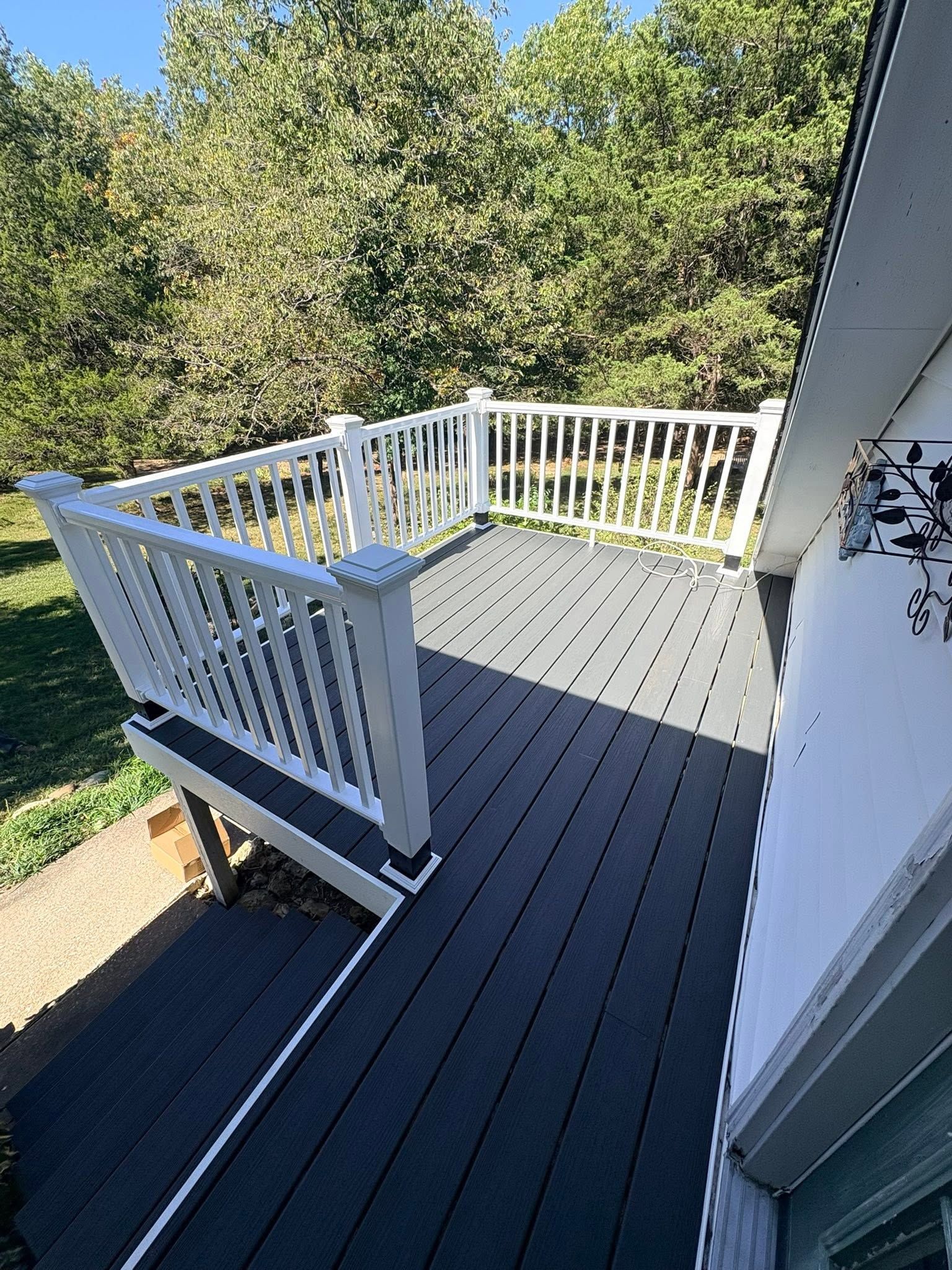 White-railed gray deck with stairs beside a house, overlooking trees and grass