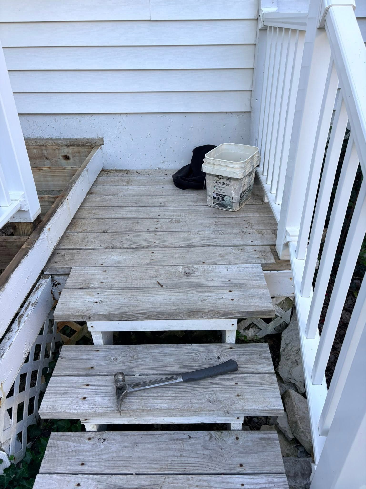 Wooden steps leading to a small weathered porch with a bucket and black bag beside it