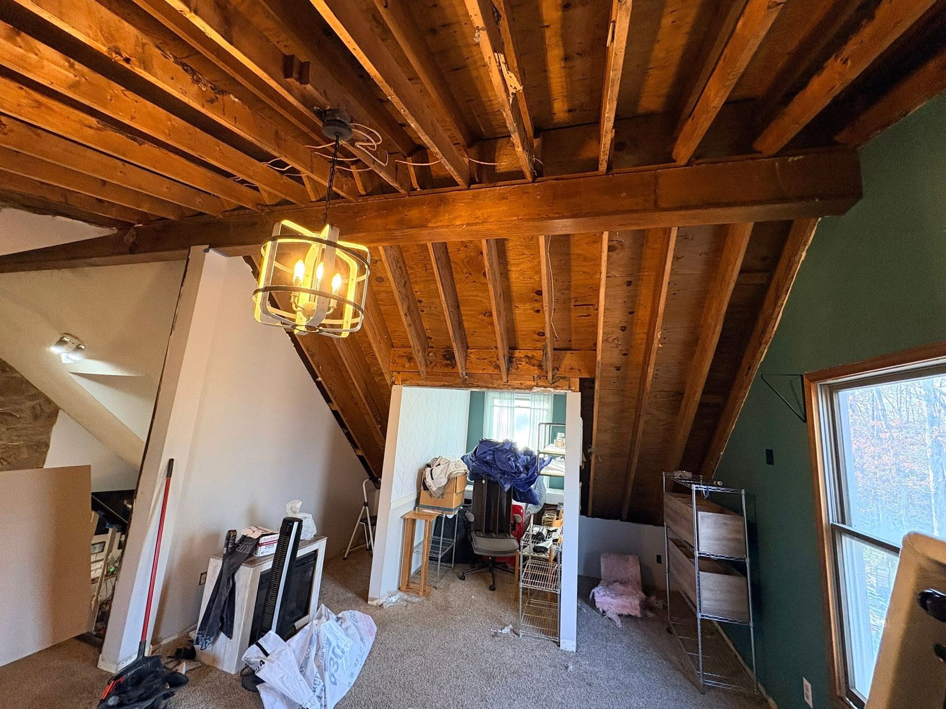 Wood-paneled hallway with exposed beams, hanging light, and an open doorway leading to a cluttered room