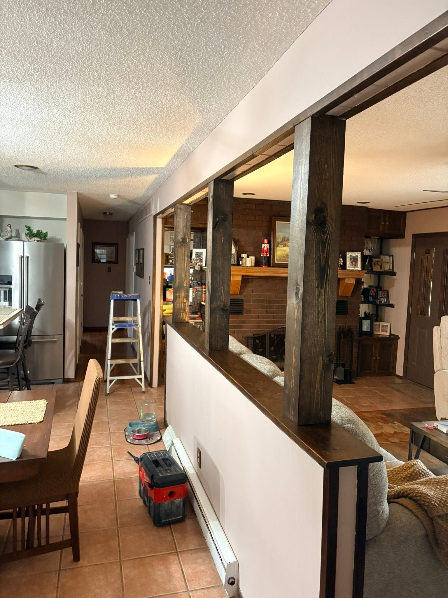 Living room and kitchen viewed through a pass-through, with a dining table, ladder, and toys on the floor.