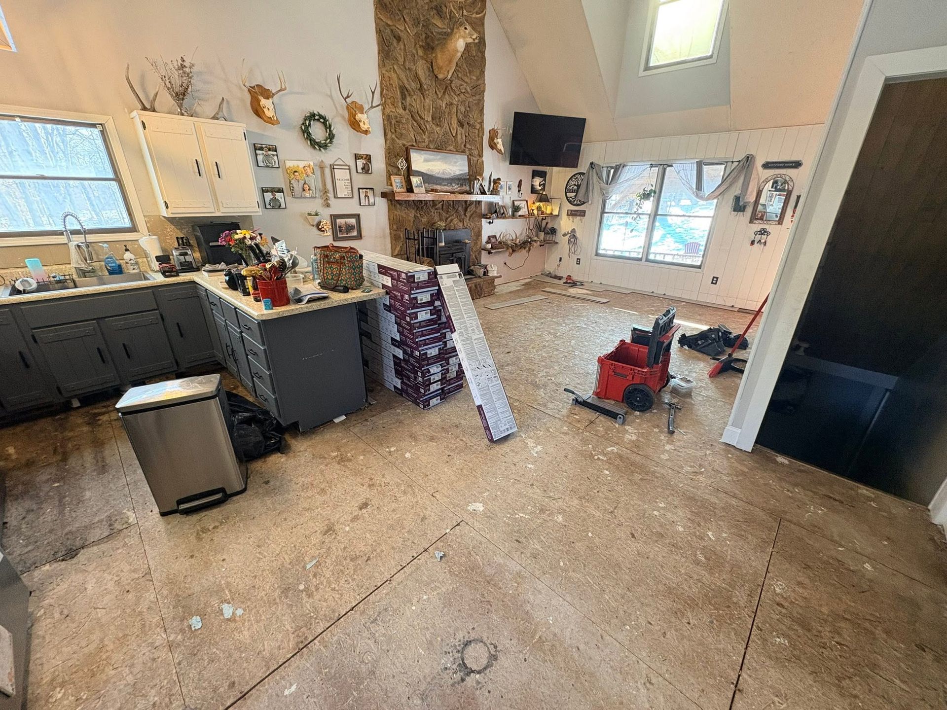 Cluttered kitchen with cabinets, tools, a black fridge, and a red snowblower on a concrete floor.
