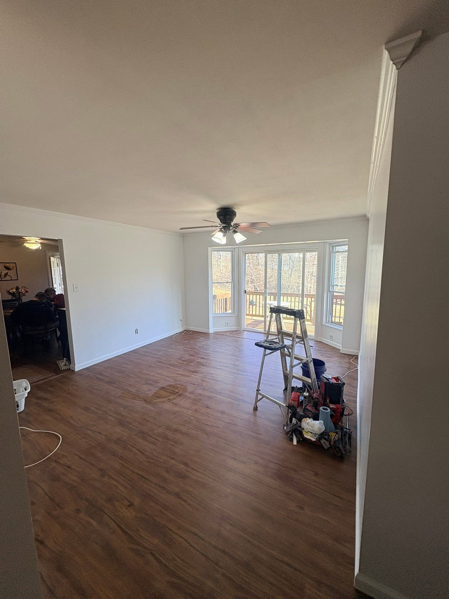 Empty living room with wood floors, white walls, and large windows letting in daylight.