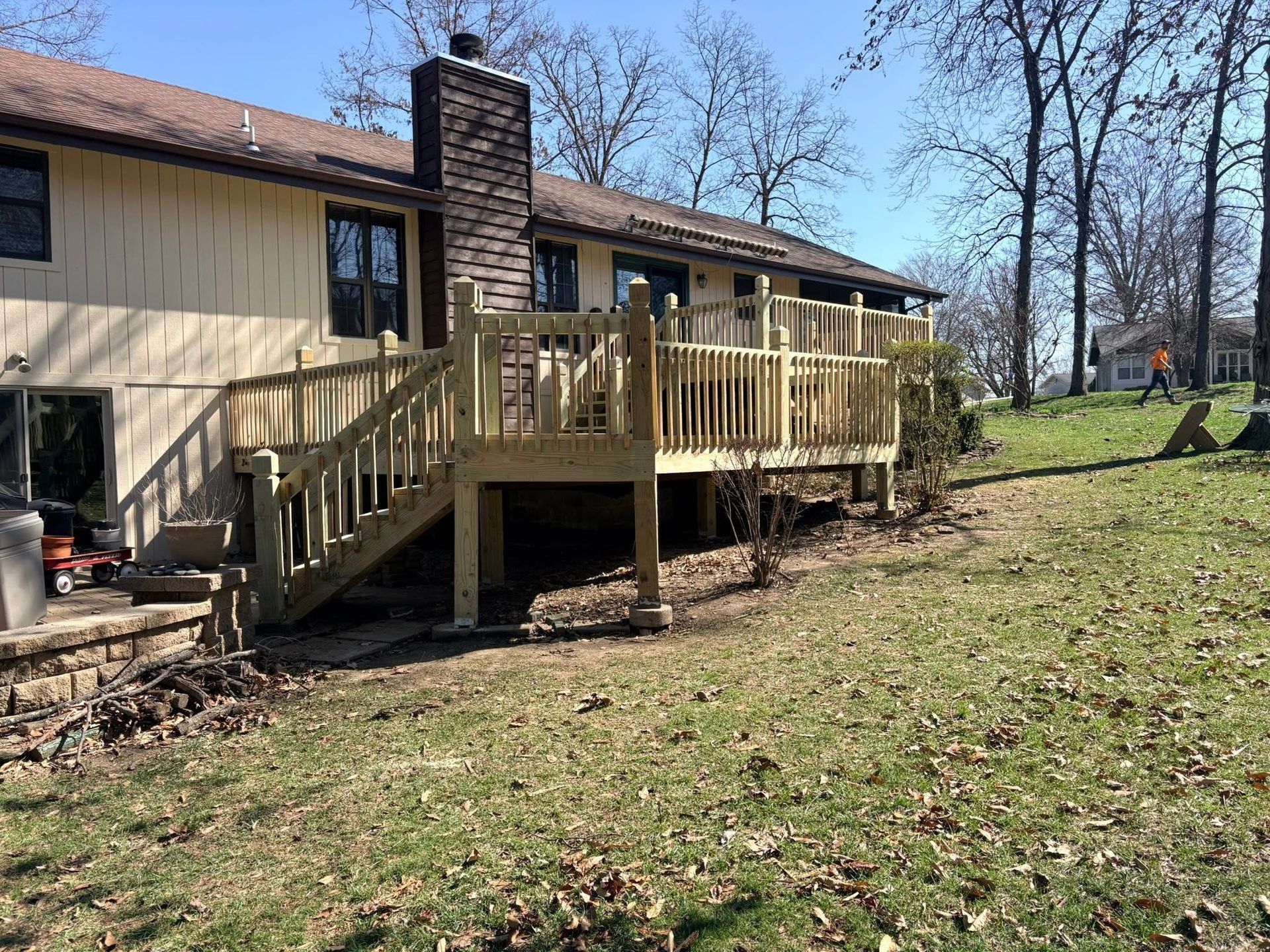 Back deck with wooden stairs beside a beige house, overlooking a grassy yard and trees