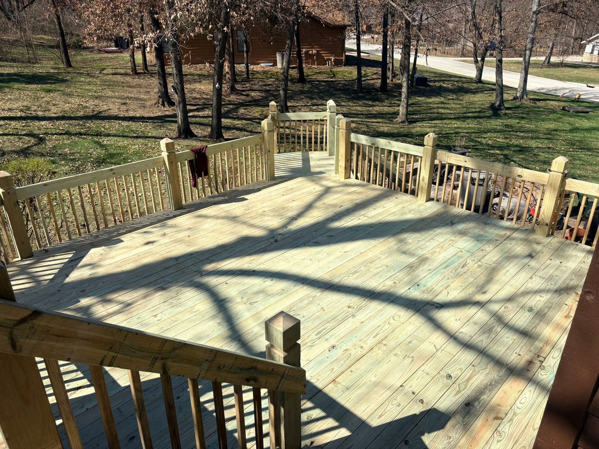 Wooden deck with railings in a park, casting long shadows across the sunlit boards.