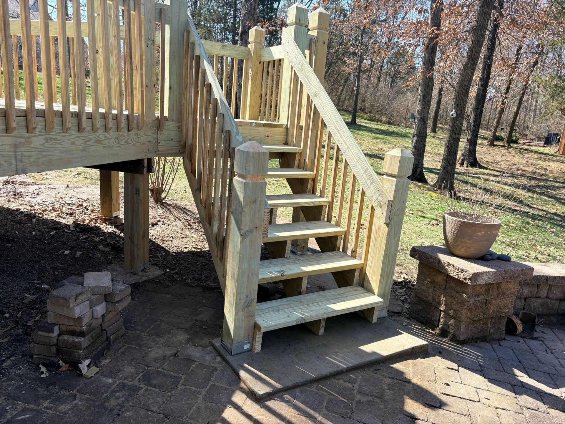Wooden outdoor staircase leading to a deck, with brick supports and potted plants nearby.