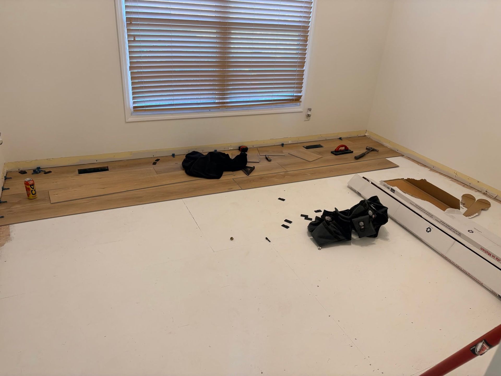 Empty room with bare floorboards, a window with blinds, and tools and debris scattered around