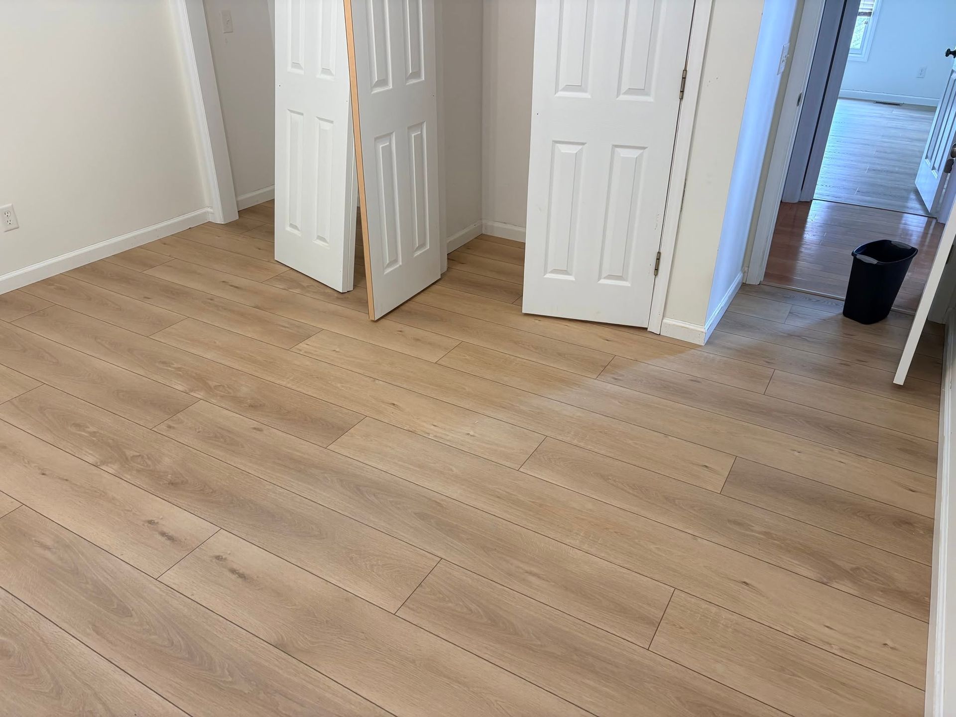 Empty room with light wood flooring, white walls, and open closet doors in the corner