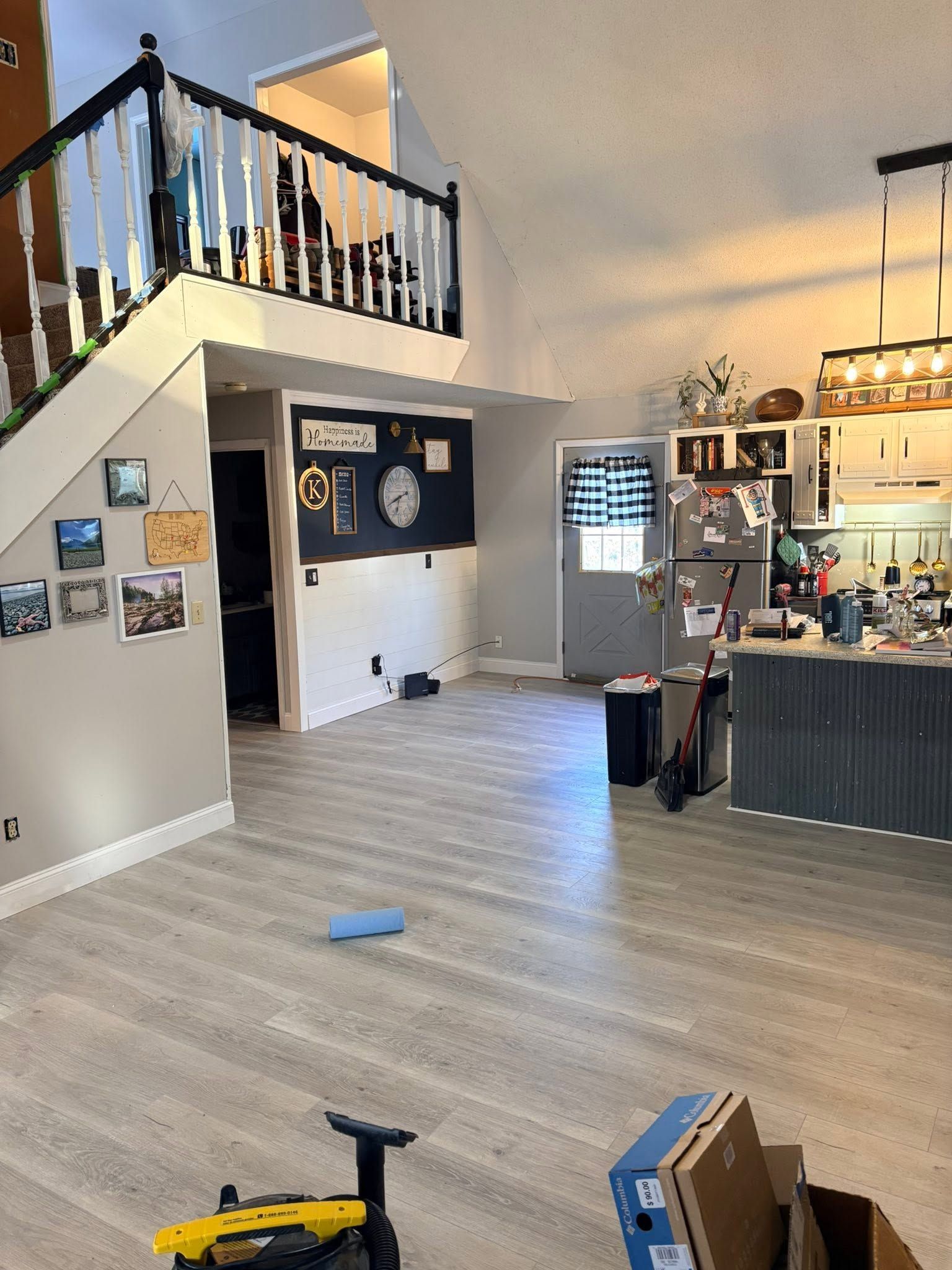 Interior of a home with staircase, open floor, wall photos, and a kitchen area on the right.