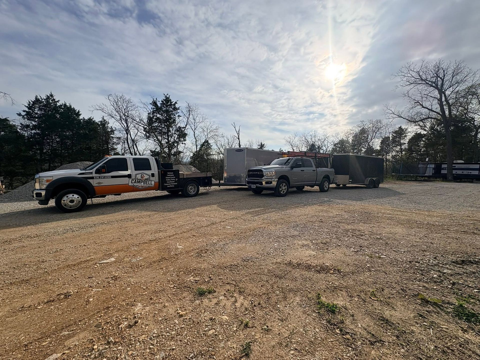 Pickup trucks and trailers parked on a gravel lot under a cloudy sky.