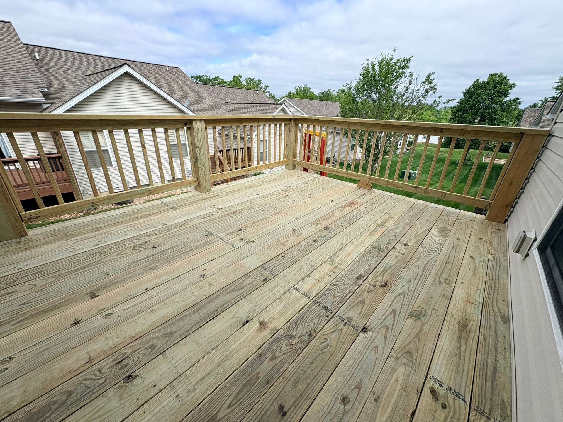 Wooden deck with railings overlooking a yard and neighboring houses