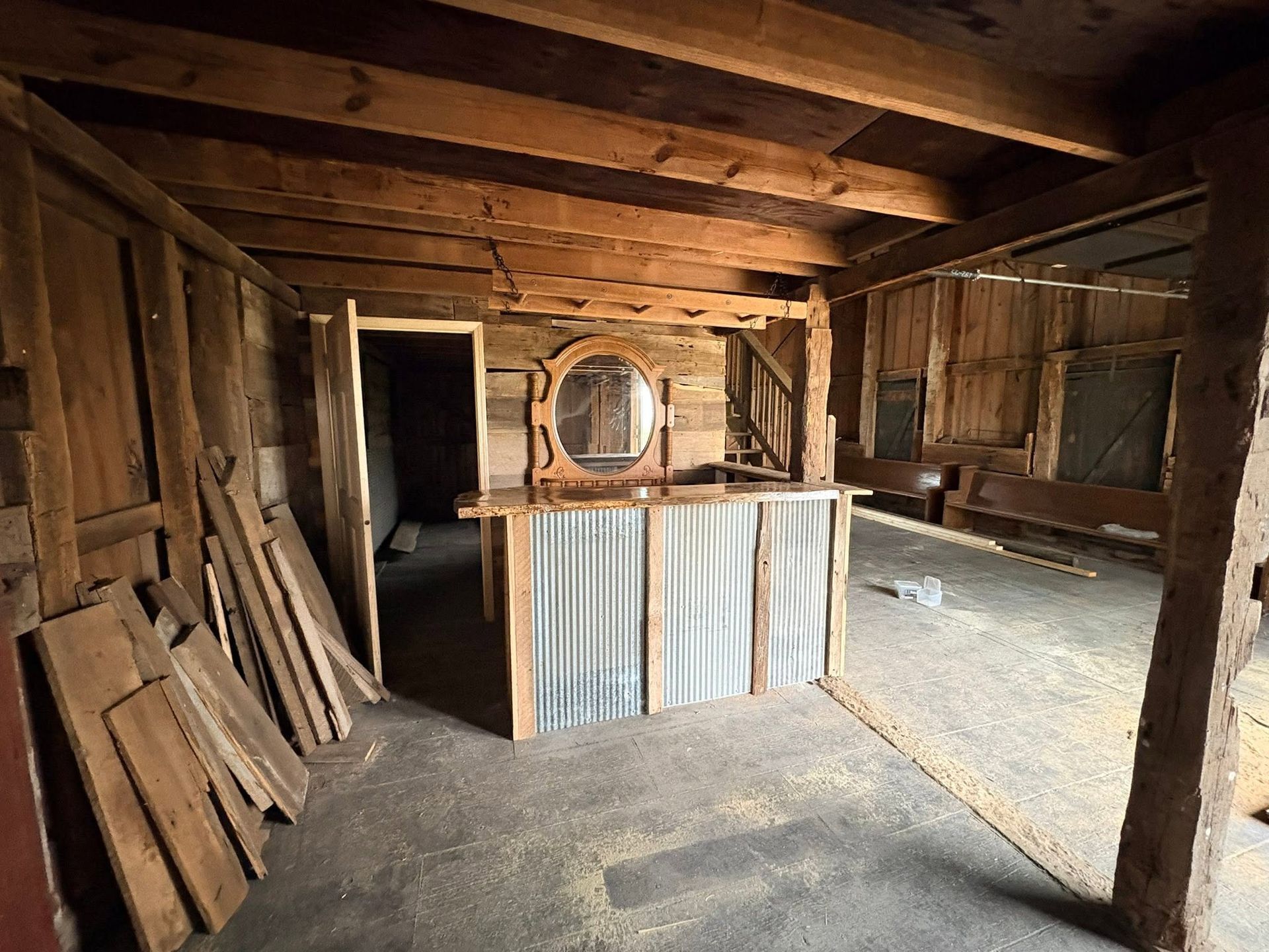 Old wooden barn interior with stacked planks, rough beams, and a corrugated metal counter in the center