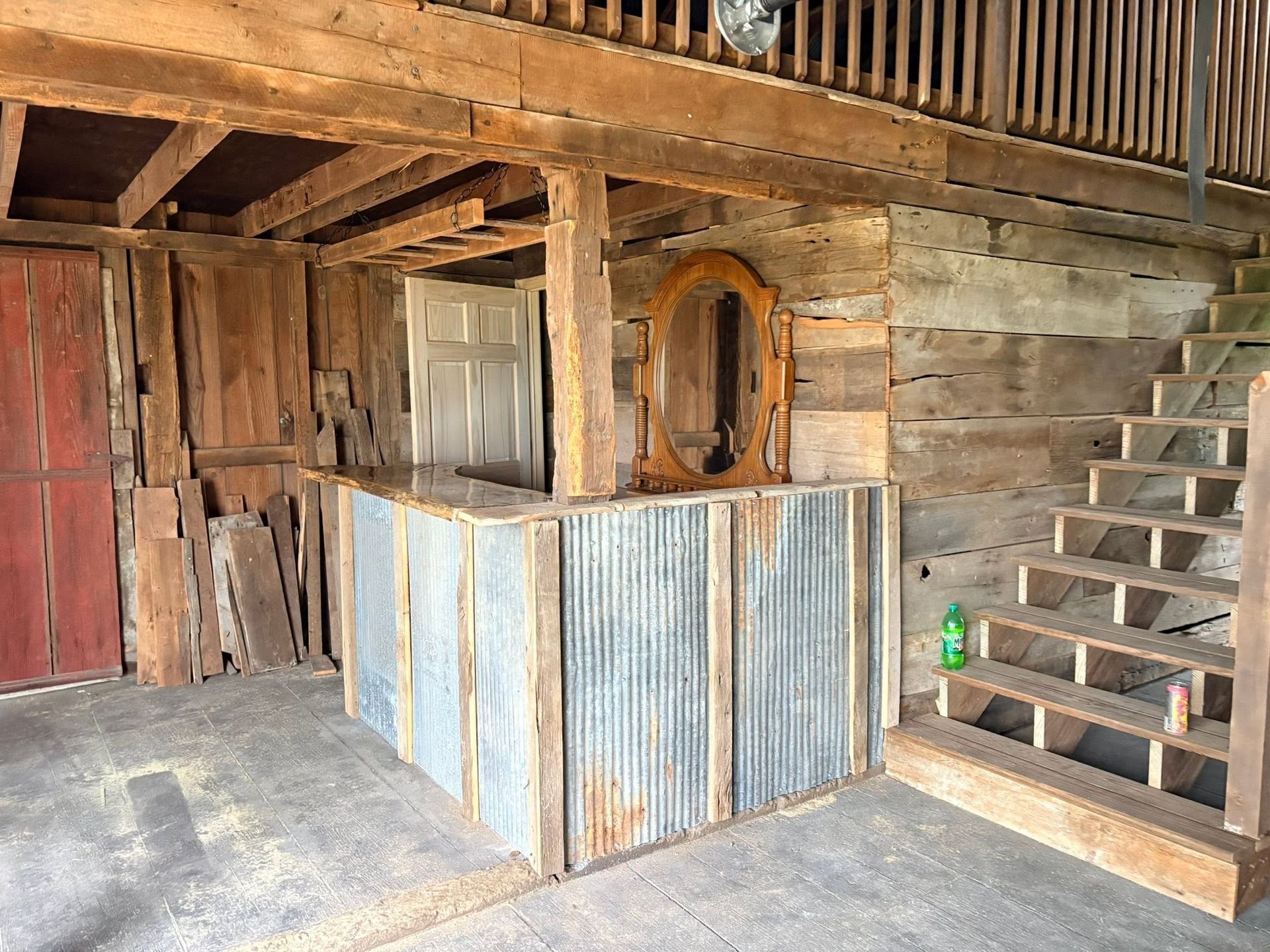 Rustic interior with corrugated metal counter, wooden stairs, and a wall mirror under a loft.