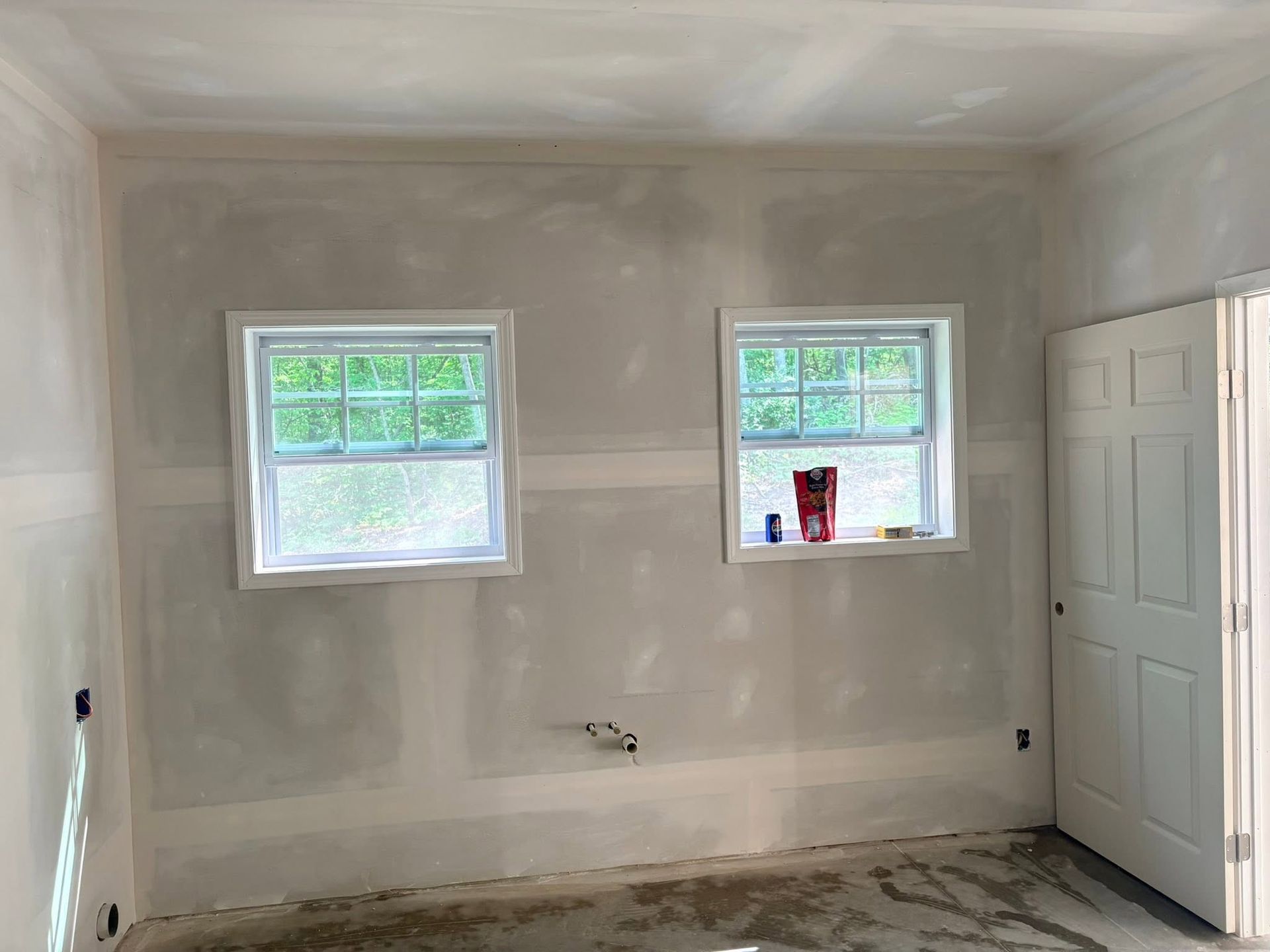 Empty room with white walls, two windows, and an open white door on the right.