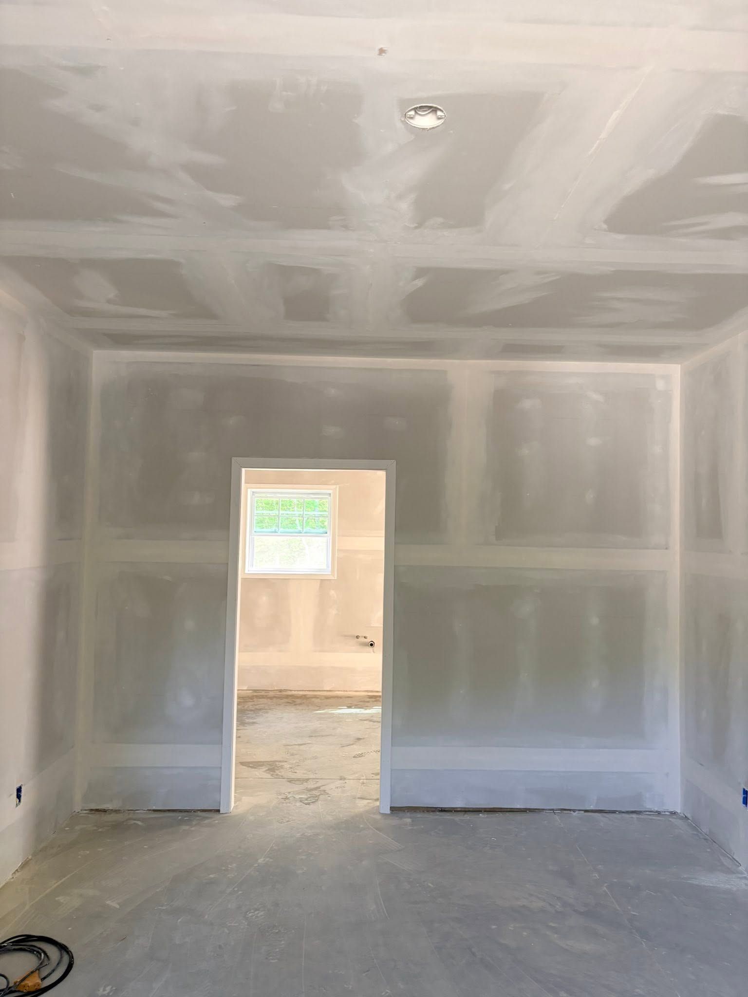 Unfinished drywall room with a doorway opening to a lit outdoor area.