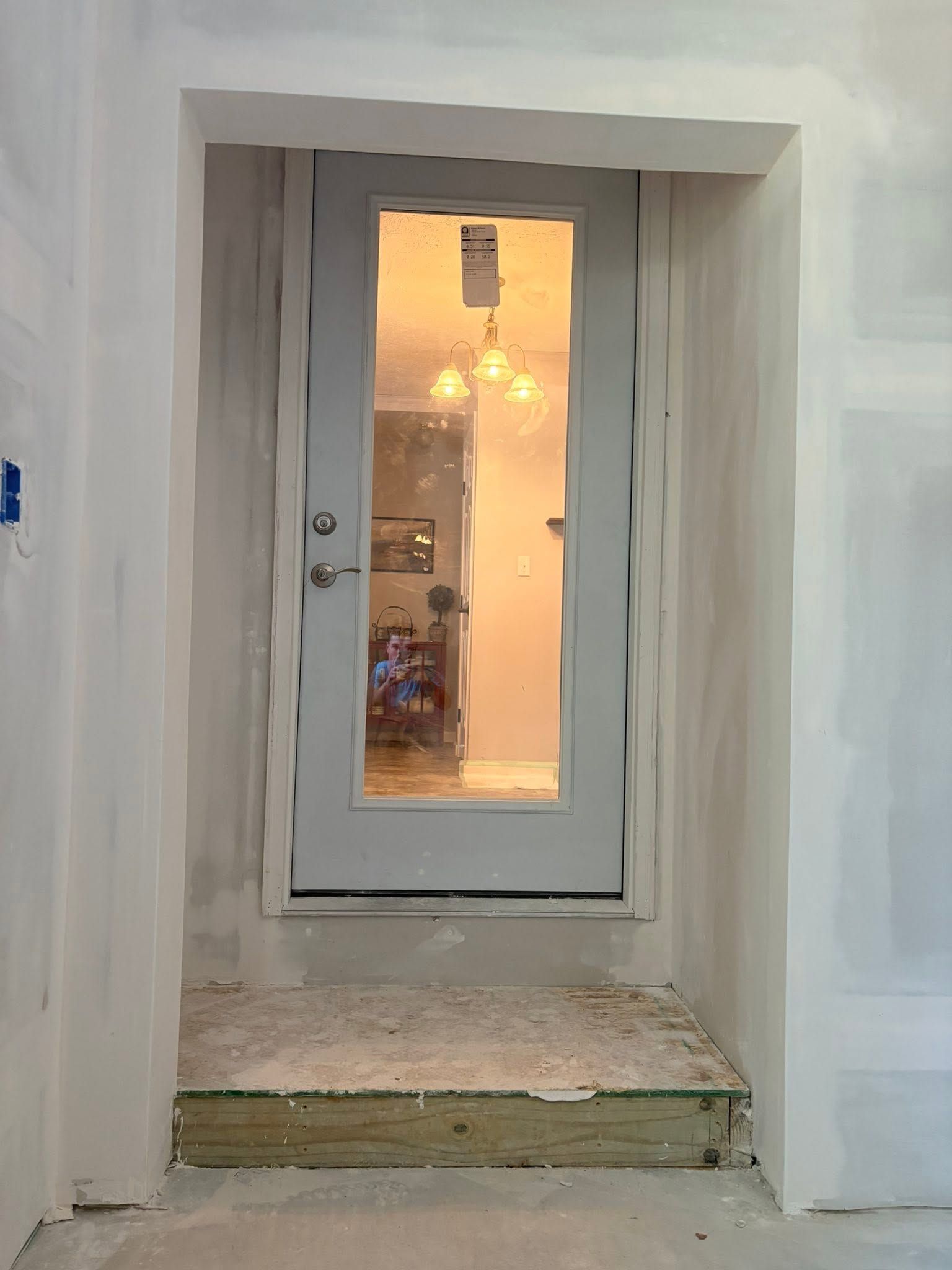 White doorway in a wall leads to a warmly lit room with a glass door and chandelier.