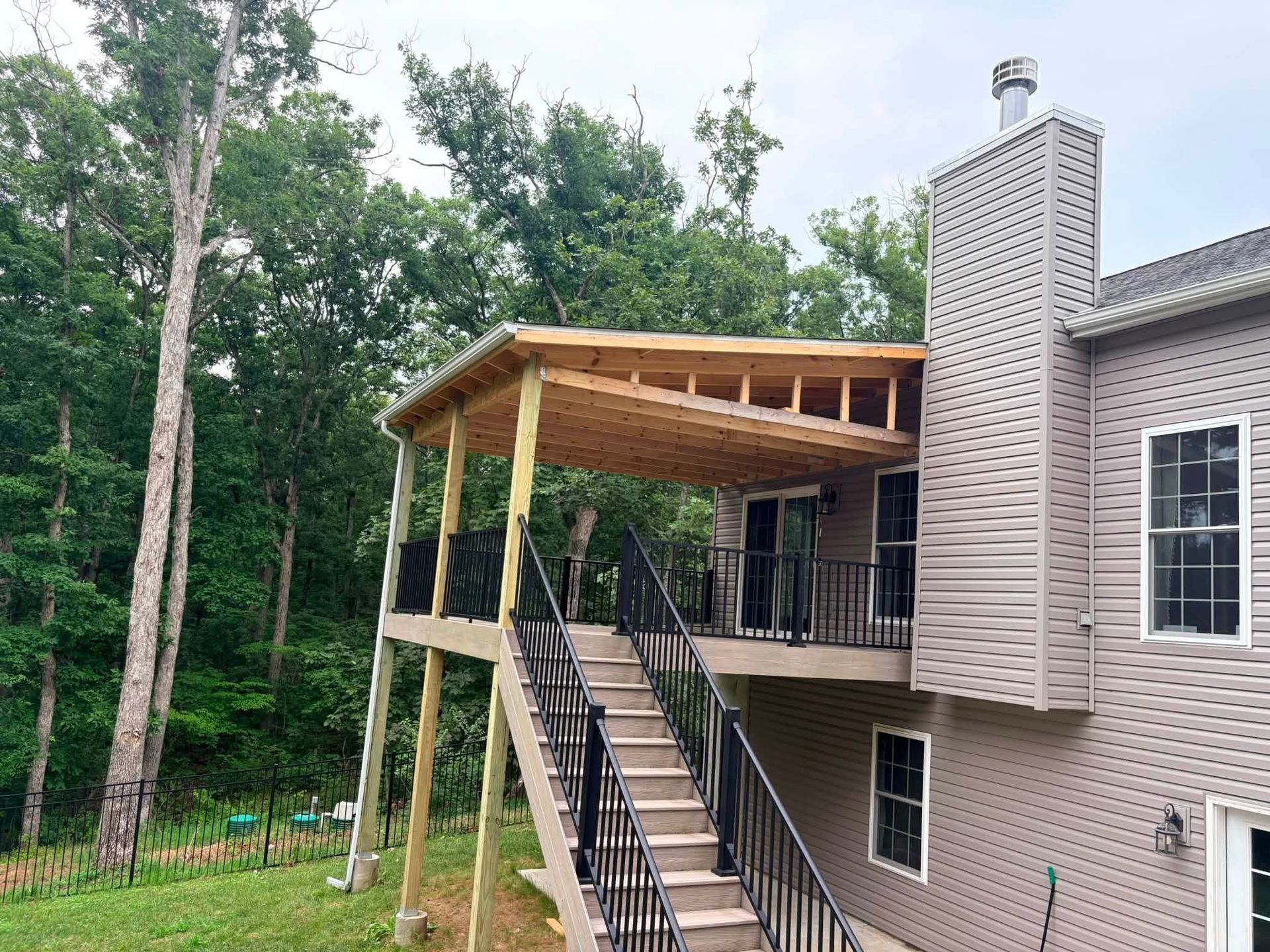 House with elevated wooden porch and stairs beside a forested yard