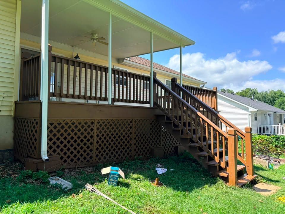 Wooden porch with stairs and railing on a house, under a green roof in a sunny yard
