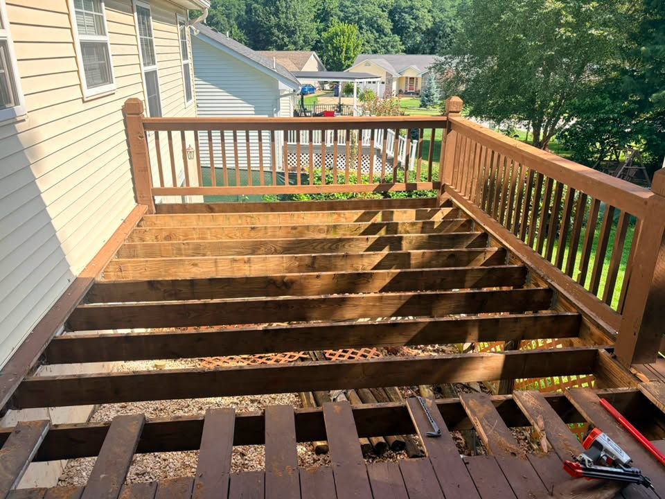 Wooden deck stairs and railing beside a beige house, overlooking a sunny backyard.