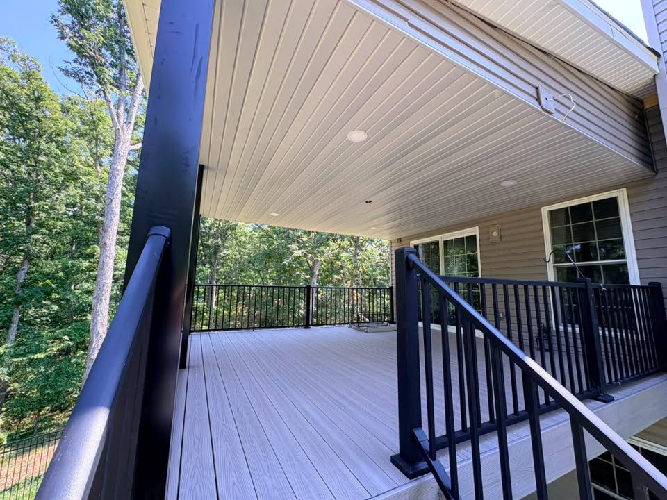 Covered wooden deck with black railings and forest view beside a house