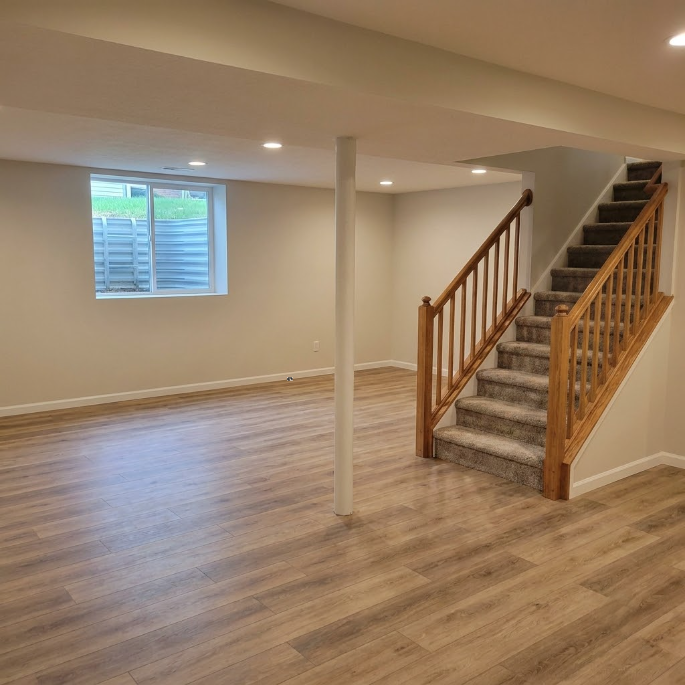 Bright living room with staircase, open floor, wall photos, and kitchen counter in the background