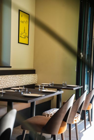 Zwei Personen unterhalten sich an einem Café-Tisch, aufgenommen durch ein Fenster mit verschwommenem Vordergrund.