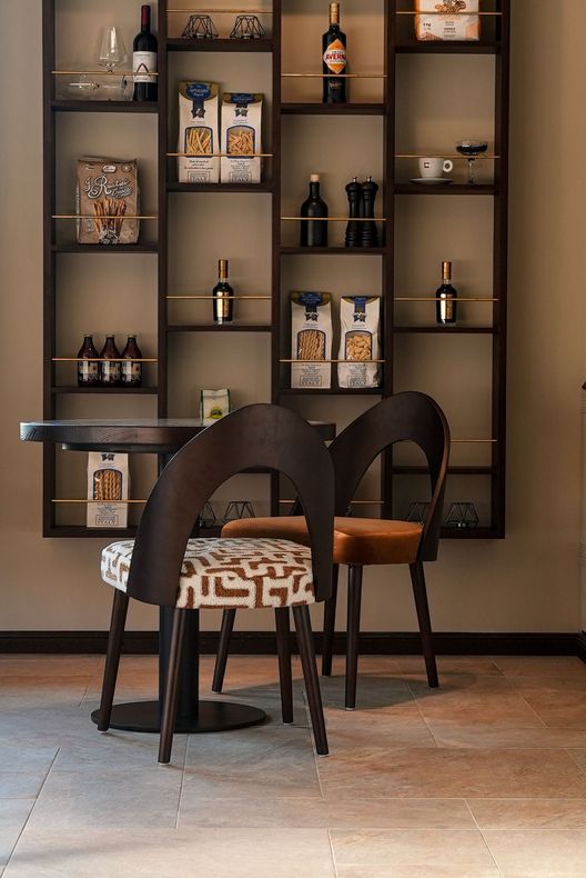 Zwei moderne Stühle in einem Café vor einer Wand mit Regalfächern, in denen Dekoration und Flaschen aufbewahrt werden.