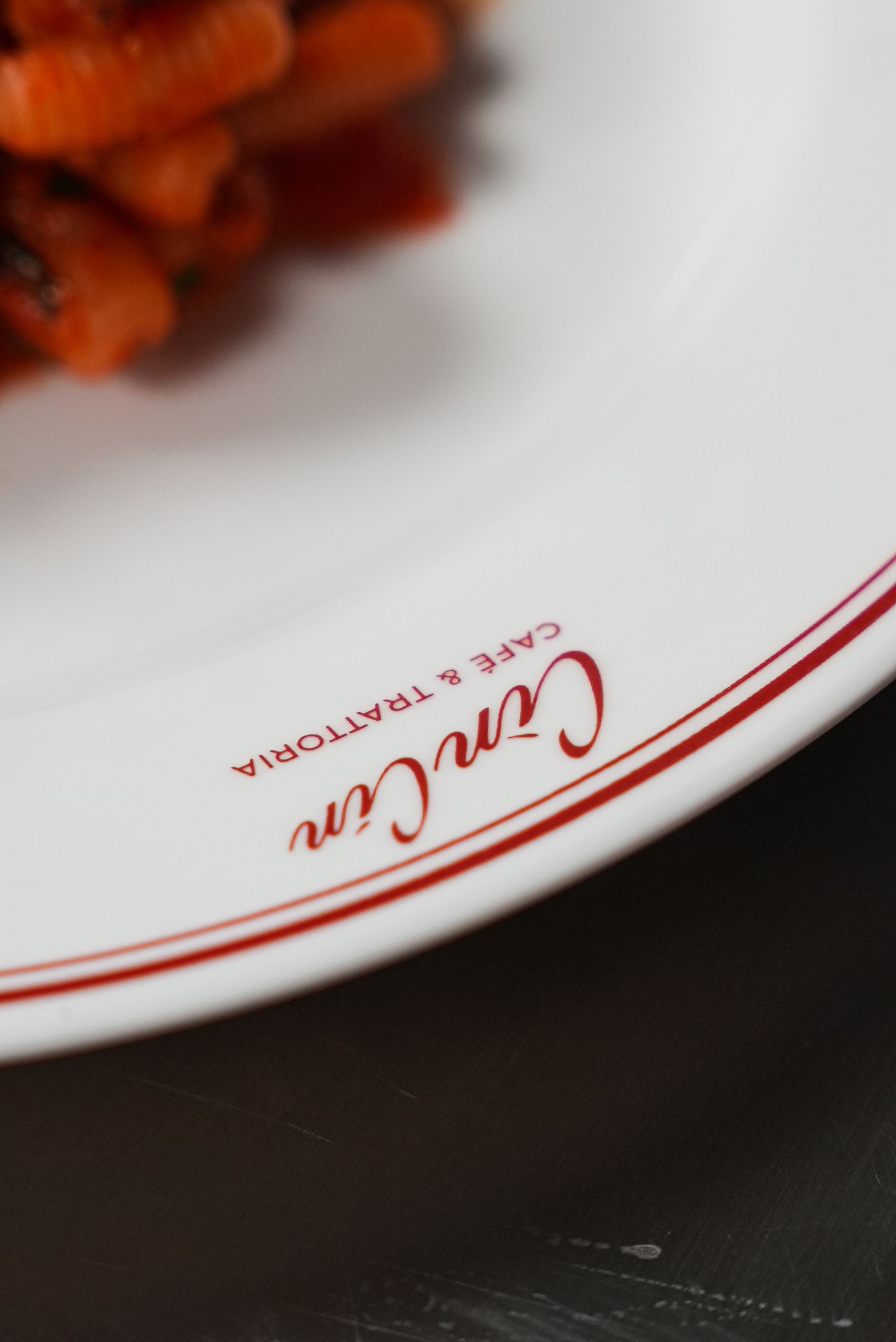 Weißer Teller mit rotem Logo, auf dem Pasta steht, auf einem dunklen Tisch