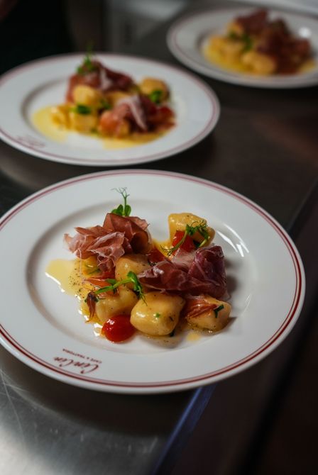 Gourmetgericht mit Fleisch, Kartoffeln und Kirschtomaten auf einem Teller mit weißem Rand.